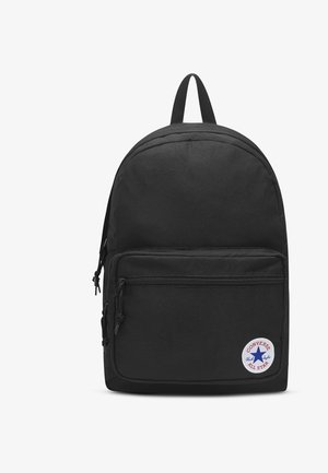 Sac à dos Converse noir avec poche zippée à l'avant et écusson rond blanc portant une étoile bleue et un texte rouge.