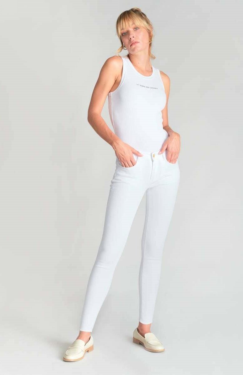 Camiseta sin mangas blanca con un pequeño texto gráfico, combinada con unos pantalones vaqueros de denim blanco ajustados y mocasines claros. Diseño simple y elegante.