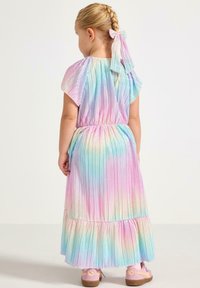 Pastel regenboog geplooide jurk met uitlopende mouwen, elastische tailleband en gelaagde zoom. Draagt roze schoenen met een bandje.
