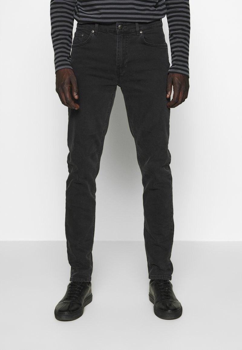 Jeans en denim noir à coupe slim, dotés d'un design classique à cinq poches, de coutures subtiles et d'une texture lisse. Assortis à des baskets noires.