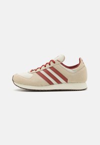 Zapatilla beige con rayas rojas, upper de ante texturizado y malla, suela de goma y cierre de cordones. Diseño retro ligero con acentos mínimos.