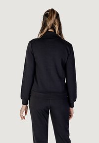 Felpa nera con maniche lunghe, tessuto testurizzato e dettagli scintillanti lungo le maniche. Polsini e orlo a costine, vestibilità comoda.