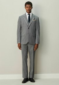 Šedý károvaný oblek s výrezovými klopami, zapínaním na jeden gombík a zúženými nohavicami. Kombinovaný s bielou košeľou, čiernou kravatou a čiernymi spoločenskými topánkami.