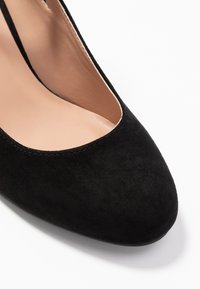 Chaussure femme en daim noir à bout rond, empeigne basse et doublure intérieure beige sur fond blanc.