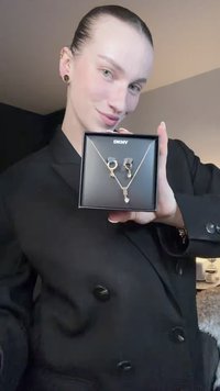 Arany tónusú DKNY ékszerszett fekete dobozban: egy nyaklánc téglalap alakú medállal és egy csepp alakú díszítéssel, valamint hozzáillő karika fülbevalók.