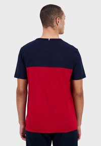 T-shirt i bomull med en marinblå överdel och röd underdel. Rund halsringning, korta ärmar och en liten flaggdetalj på baksidan.