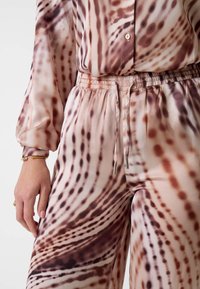 Seidenblusen- und Hosen-Set mit einem fließenden, wellenartigen Muster in Beige- und Brauntönen. Elastischer Bund mit Kordelzugdetail.