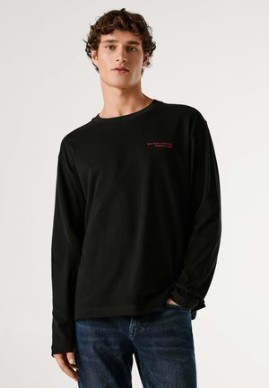 Maglietta nera a maniche lunghe con scollo a girocollo, con scritta rossa sul petto. Realizzata in morbido cotone, abbinata a jeans blu.