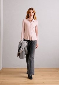 Lyserosa skjorte med lange ermer, parret med mørkegrå vide jeans. Modellen holder en grå rutete blazer. Sorte ankelstøvler.