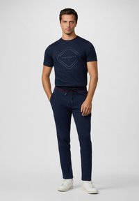 Marinblå grafisk t-shirt med diamantlogotyp, kombinerad med marinblå joggbyxor med röd och blå randig midja. Vita sneakers.