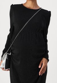 Robe noire à manches longues, en tissu texturé, avec une taille froncée. Assortie à un sac à bandoulière argenté avec un design géométrique.