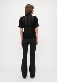 Blusa nera in pizzo con maniche corte, colletto e texture a motivo. Abbinata a pantaloni neri a vita alta e svasati.