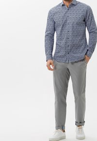 Camicia blu con bottoni, decorata con un motivo floreale bianco, abbinata a pantaloni grigi chiari e sneakers bianche. Vestibilità casual, maniche lunghe e colletto piatto.