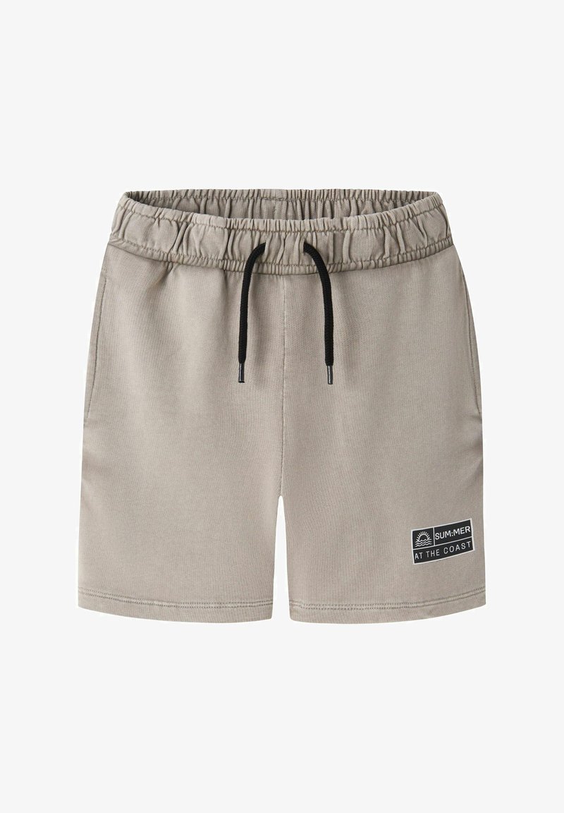 Short beige à taille élastique avec cordon noir et poches latérales, avec un patch « SUM:MER AT THE COAST » sur la jambe gauche.