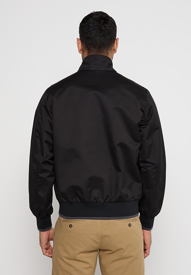 Schwarze Bomberjacke mit hohem Kragen und gerippten Bündchen. Hergestellt aus glattem, leichtem Stoff. Verfügt über eine taillierte Passform und minimale Nähdetails.
