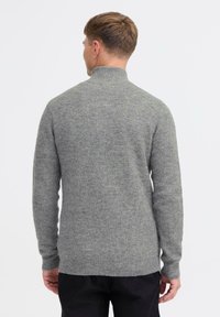 Grijze gebreide trui met een hoge kraag, ribbeltextuur en lange mouwen. De achterkant heeft een rechte snit met een iets afgeronde zoom.