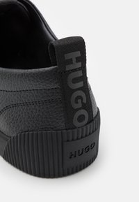 Schwarze Ledersneaker mit strukturiertem Finish und Gummisohle. Die Rückseite hat eine gewebte Schlaufe mit dem in fetten Buchstaben aufgedruckten "HUGO".