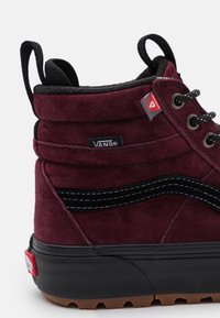 Burgunderfarget semsket høyhælte sneakers med svarte detaljer, kontrasterende sømmer, runde snøring, og en strukturert gummisåle. Har et Vans-logoet mærke.