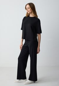 Zwarte korte mouwen top met een loose fit, gecombineerd met hoge zwarte wijde broek, aangevuld met witte sneakers. Glad stoffen textuur.
