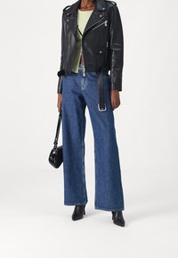 Černá kožená motorkářská bunda se stříbrnými detaily, světle zelený žebrovaný top, široké modré džíny a černé boty na podpatku. Součástí je černá kabelka.