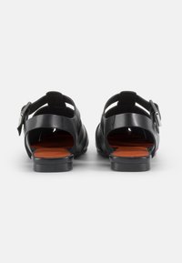 Black leather sandals featuring an open back, two adjustable straps, and a smooth orange insole with a low black heel.