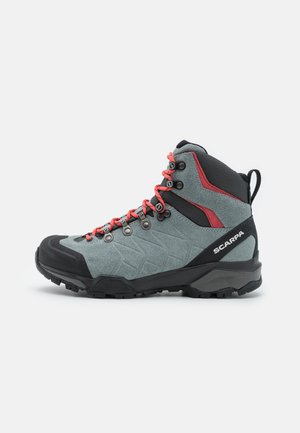 Vandretningsstøvle i grå ruskind med røde snørebånd, sorte accenter og en tekstureret gummisål med et hexagonalt mønster samt forstærket tåhætte.