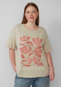 Beżowa bawełniana koszulka z krótkimi rękawami, ozdobiona kwiatowym nadrukiem w kolorze koralowym i białym. Na dole znajduje się napis "LES FLEURS".