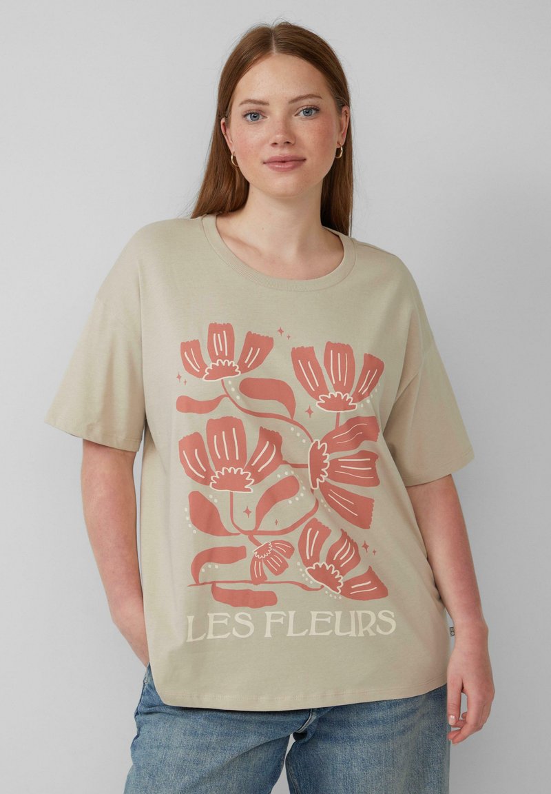 Beżowa bawełniana koszulka z krótkimi rękawami, ozdobiona kwiatowym nadrukiem w kolorze koralowym i białym. Na dole znajduje się napis "LES FLEURS".