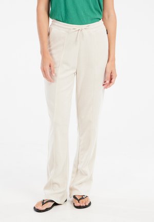 Beige fleece pants with a drawstring waist, straight leg design, and side seams. Worn with black flip-flops and a green top.