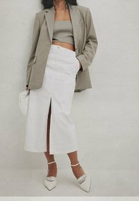 Light gray oversized blazer paired with a fitted gray crop top and a white pencil skirt featuring a front slit. Woven white heeled shoes.