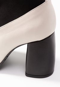 Krémová a černá bloková jehla s hladkým, texturovaným povrchem. Disponuje kontrastní patou a strukturovaným designem.