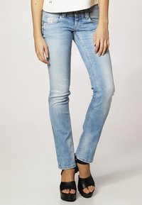 Jeans skinny de color azul claro con un efecto desgastado, diseño de cinco bolsillos y una etiqueta en la cinturilla. Combinados con sandalias negras de plataforma.