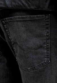 Posnetek v bližini črnega džinsovskega zadnjega žepa z vidnim šivom in delom črne usnjene jakne nad njim.