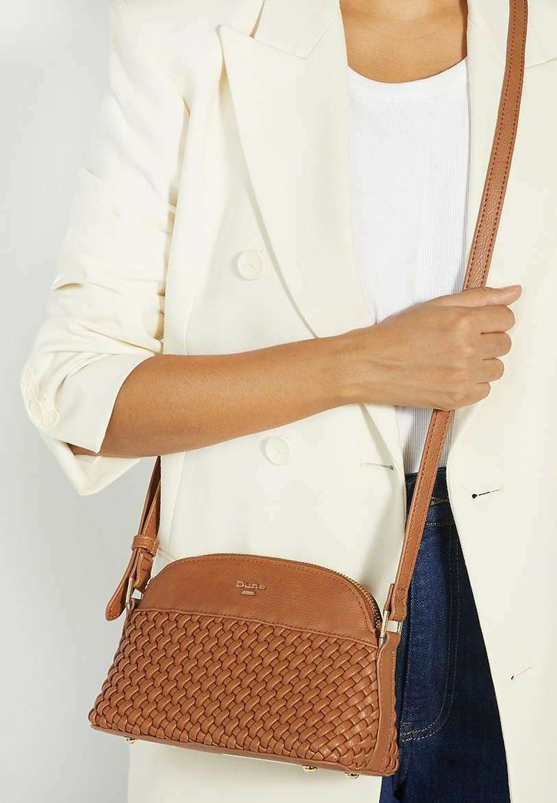 Tan woven leather crossbody bag with a smooth top, adjustable strap, and subtle branding, displayed against a light background.