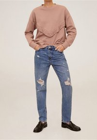 Jasnoróżowy sweter z falbaną u dołu, w połączeniu z niebieskimi dżinsami z przetarciami i wieloma dziurami. Całość dopełniają czarne mokasyny.