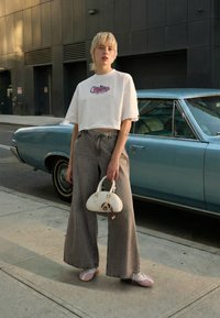 Tricou alb scurt cu text grafic, blugi gri cu talie înaltă și croială largă, balerini roz deschis și o geantă albă cu detaliu de breloc.