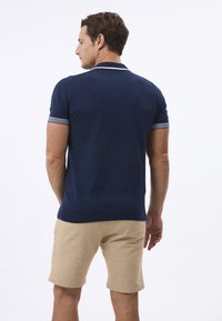 Marineblaues Poloshirt mit kurzen Ärmeln und weißen Akzenten am Kragen und an den Ärmeln, kombiniert mit beigen Shorts. Glatte Textur, lässige Passform.