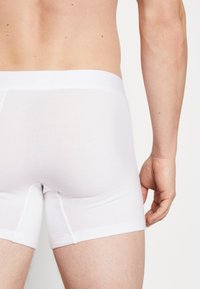 Weiße Baumwollboxershorts mit glatter Textur und breitem elastischem Bund, ausgestattet mit einem kurzen Beinausschnitt und einfachem Design.