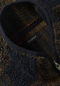 Giacca in pile marrone e nera con texture, con zip frontale e un'etichetta del marchio "Martinique" visibile all'interno del colletto.