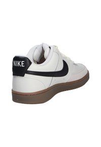 Zapatilla de cuero blanca con logotipo y acentos negros de Nike, upper texturizado, punta redondeada y suela de goma, diseñada para uso casual.