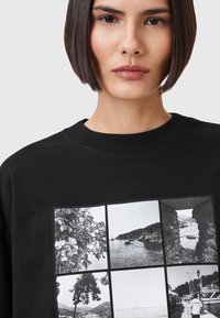 Sudadera negra con un diseño de una cuadrícula de seis impresiones en blanco y negro, que representan escenas florales, costeras y arquitectónicas.