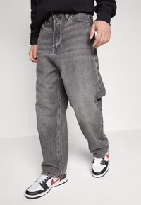 Šedé džínové džíny s volným střihem, vysokým pasem a výraznými kapsami, doplněné černo-bílými teniskami s červenými detaily.