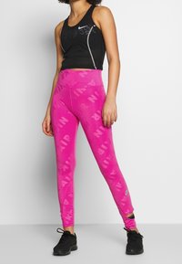 Top in cotone nero Nike con logo e dettagli riflettenti, abbinato a leggings rosa con grande stampa bianca "AIR". Design testurizzato e aderente.