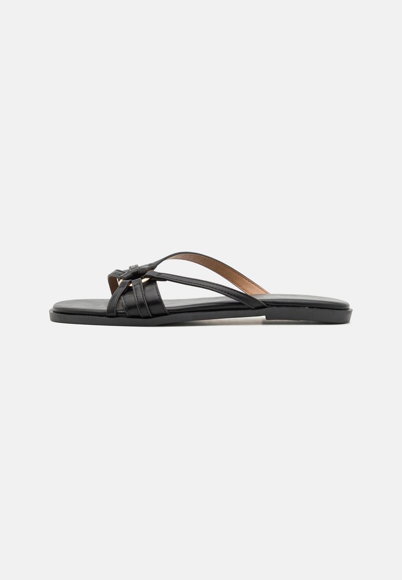 Sandales en cuir noir à tongs avec de fines lanières croisées et une semelle plate, arborant un design minimaliste et une texture lisse.