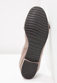 Stivaletto in suede beige chiaro con suola in gomma nera testurizzata. Presenta una punta rotonda e una finitura liscia sulla parte superiore.