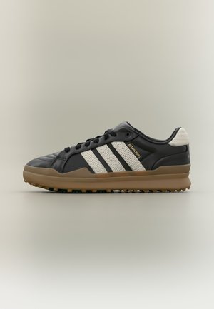 Μαύρο και μπεζ παπούτσι Adidas Retro Cross με σόλα από καουτσούκ και λευκό σχέδιο με τρεις ρίγες, παρουσιάζεται σε ουδέτερο φόντο.