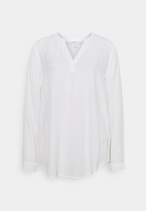 Camicia bianca a maniche lunghe in un tessuto leggero. Presenta una scollatura a V, dettaglio con bottoni al collo e polsini arrotolati, con un orlo leggermente curvo.