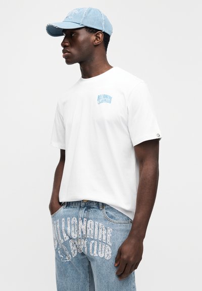 Άσπρη κοντομάνικη μπλούζα με μπλε λογότυπο "Billionaire Boy Club". Ανοιχτό μπλε καπέλο μπέιζμπολ με φθορές. Ανοιχτό μπλε τζιν με λευκές λεπτομέρειες.