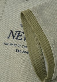 Oliwkowa koszulka polo z krótkim rękawem o teksturowanej tkaninie z haftem "NEW YORK" w ciemnoniebieskim kolorze. Posiada prążkowany kołnierz i wykończenia rękawów.