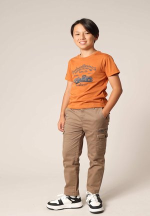 T-shirt orange avec un motif de camion, pantalons cargo khaki avec poches latérales et baskets noires et blanches. Texture lisse, coupe décontractée.